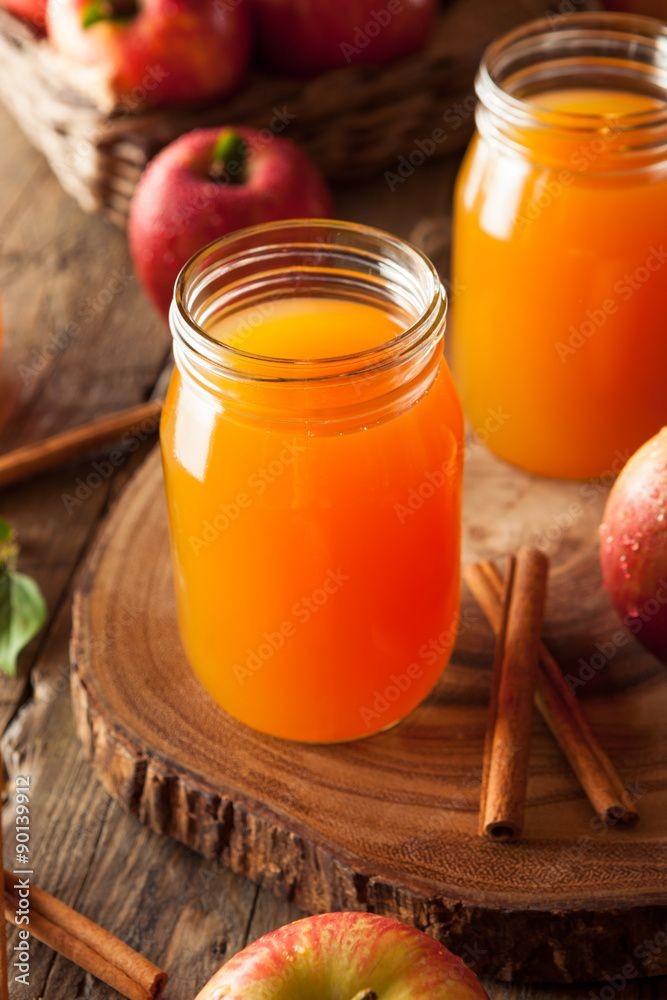 Two jars filled with fresh apple juice placed on a wooden surface with apples and cinnamon sticks around.